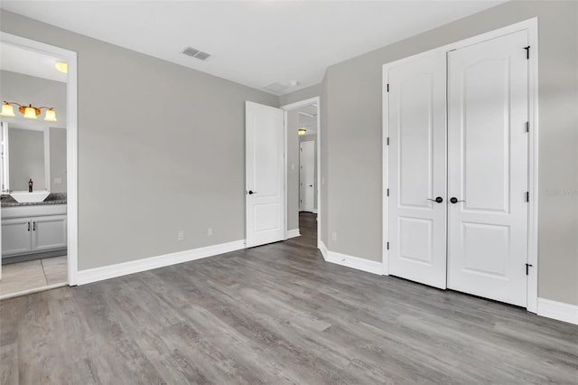 unfurnished bedroom featuring light wood-type flooring, ensuite bath, and sink