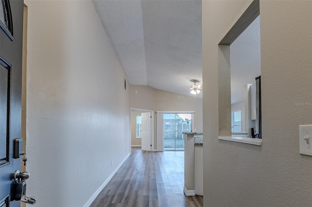 hall with hardwood / wood-style flooring, a textured ceiling, and vaulted ceiling