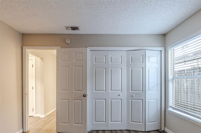 unfurnished bedroom with a textured ceiling, light wood-type flooring, and a closet