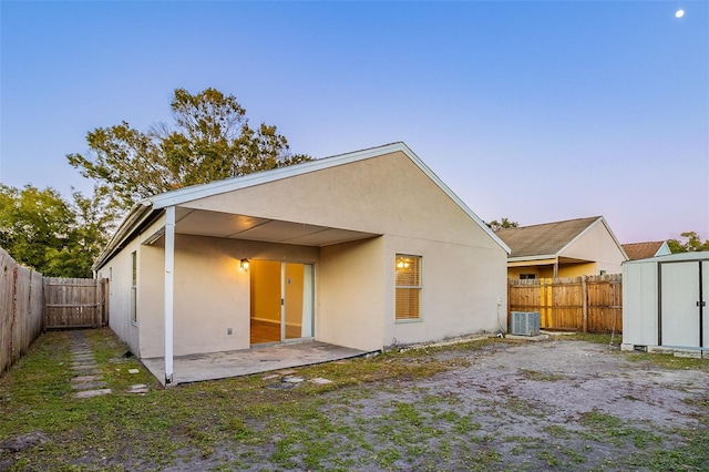 back house at dusk with cooling unit, a storage shed, and a patio