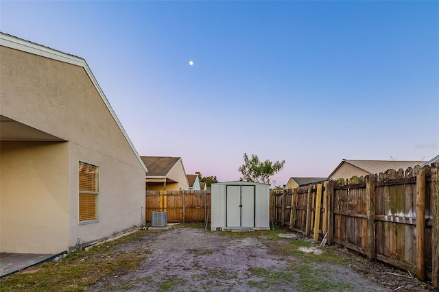 yard at dusk featuring a shed and central AC