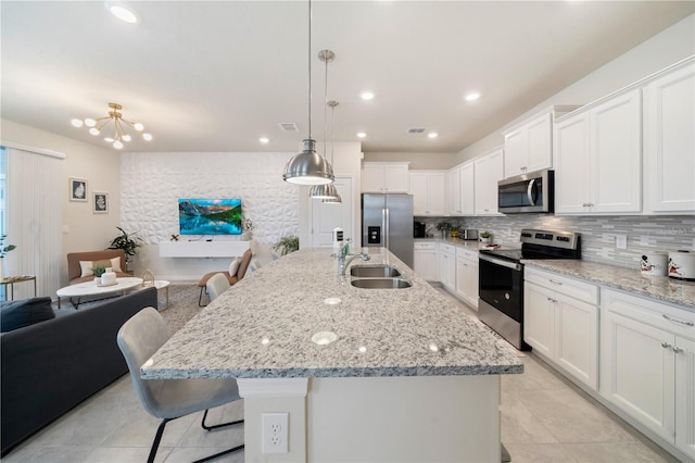 kitchen with stainless steel appliances, decorative light fixtures, a center island with sink, white cabinetry, and a breakfast bar area