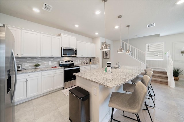 kitchen featuring a center island with sink, white cabinets, hanging light fixtures, and appliances with stainless steel finishes