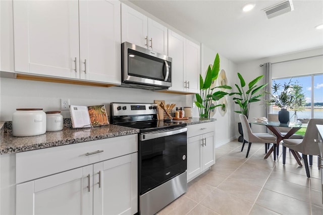 kitchen with dark stone countertops, white cabinets, stainless steel appliances, and light tile patterned floors