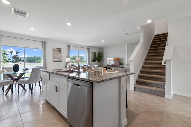 kitchen with stainless steel dishwasher, a kitchen island with sink, sink, dark stone countertops, and white cabinetry