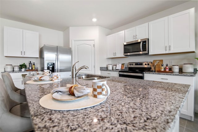 kitchen with light stone countertops, appliances with stainless steel finishes, white cabinetry, and sink