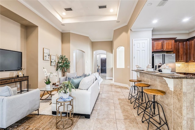 living room with a tray ceiling, light tile patterned floors, and ornamental molding