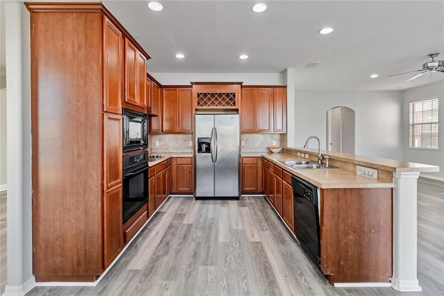 kitchen with kitchen peninsula, light wood-type flooring, tasteful backsplash, sink, and black appliances