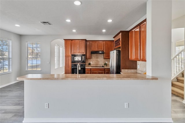 kitchen featuring black appliances, kitchen peninsula, backsplash, and light hardwood / wood-style flooring