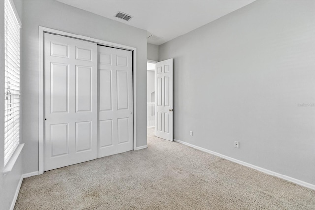 unfurnished bedroom featuring multiple windows, a closet, and light colored carpet