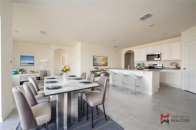 dining area with light tile patterned floors, visible vents, and arched walkways