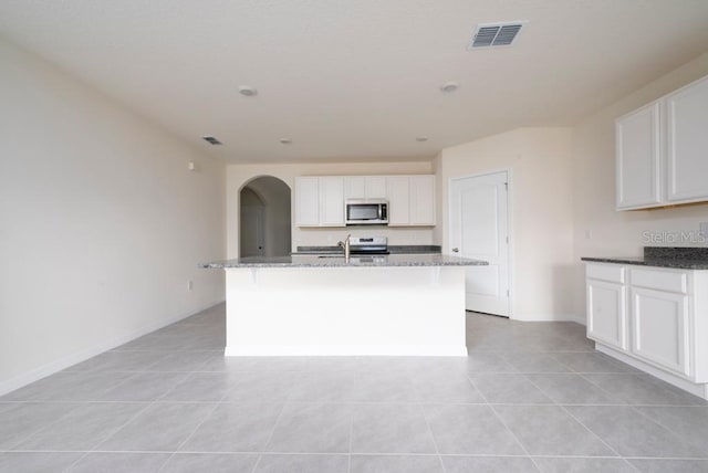 kitchen featuring arched walkways, stainless steel appliances, dark stone countertops, and visible vents