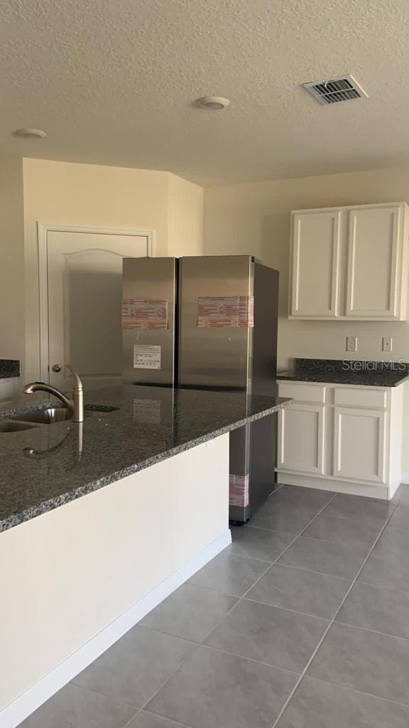 kitchen with visible vents, freestanding refrigerator, white cabinetry, a sink, and dark stone counters