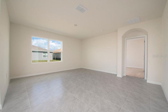 empty room with light tile patterned floors, baseboards, visible vents, and arched walkways