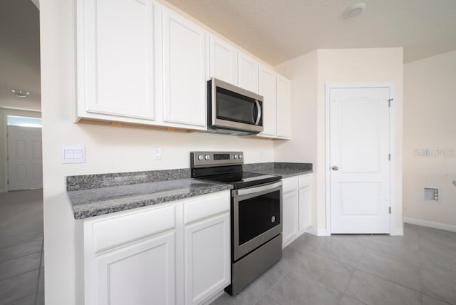 kitchen with light tile patterned floors, white cabinetry, baseboards, appliances with stainless steel finishes, and dark stone counters