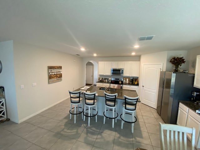 kitchen featuring light tile patterned floors, visible vents, a kitchen breakfast bar, arched walkways, and appliances with stainless steel finishes