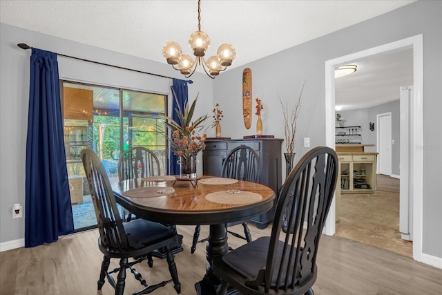 dining space with light wood-type flooring, a textured ceiling, and a notable chandelier