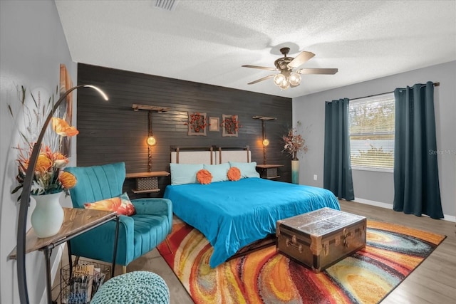 bedroom with wood walls, hardwood / wood-style floors, ceiling fan, and a textured ceiling