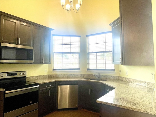 kitchen with sink, appliances with stainless steel finishes, a notable chandelier, light stone counters, and dark brown cabinetry