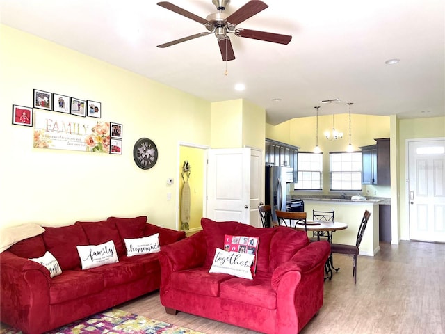 living room featuring ceiling fan with notable chandelier and light hardwood / wood-style flooring