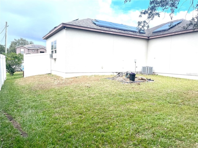 back of house featuring a lawn, central AC unit, and solar panels