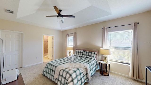 bedroom with light carpet, a raised ceiling, ensuite bath, and ceiling fan