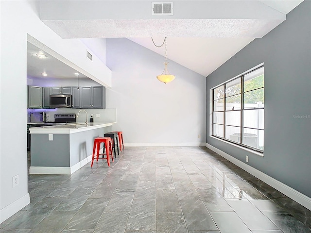 kitchen with stainless steel appliances, vaulted ceiling, hanging light fixtures, gray cabinets, and a breakfast bar