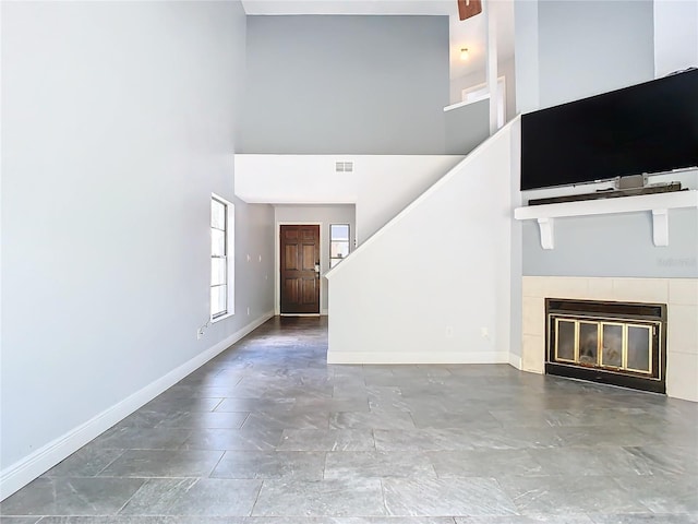 unfurnished living room with a tiled fireplace and a towering ceiling