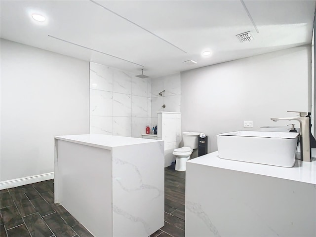 bathroom featuring toilet, a tile shower, and sink