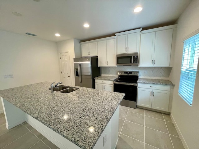 kitchen with decorative backsplash, stainless steel appliances, white cabinetry, and an island with sink