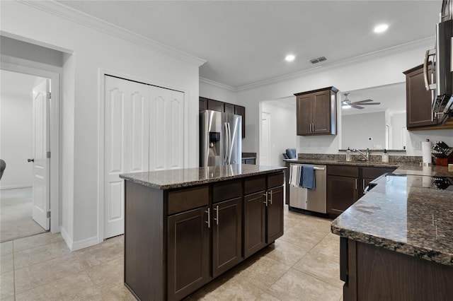 kitchen featuring appliances with stainless steel finishes, dark brown cabinets, crown molding, dark stone countertops, and a center island