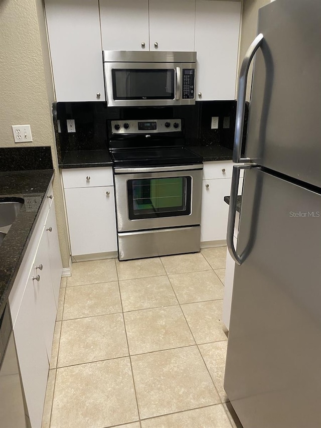 kitchen featuring dark stone counters, white cabinetry, light tile patterned floors, and stainless steel appliances