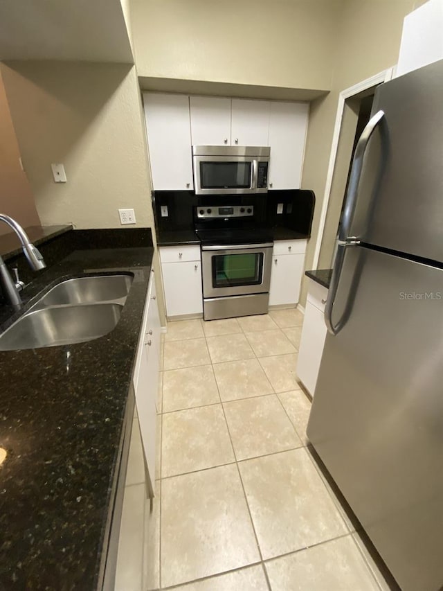 kitchen featuring sink, stainless steel appliances, light tile patterned floors, dark stone countertops, and white cabinets