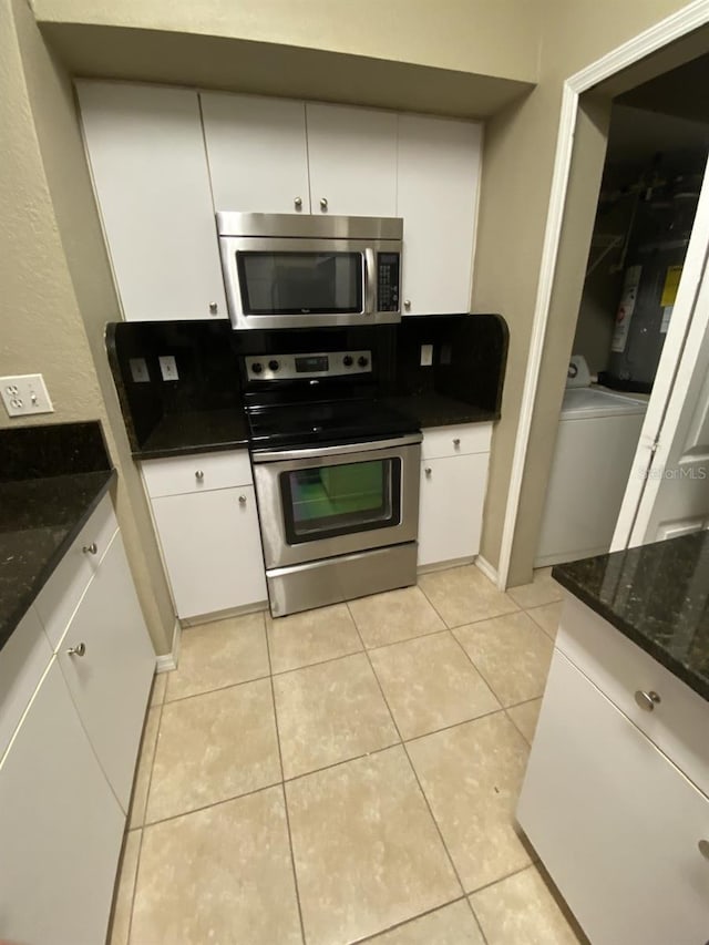 kitchen with appliances with stainless steel finishes, white cabinetry, washer / dryer, and light tile patterned flooring