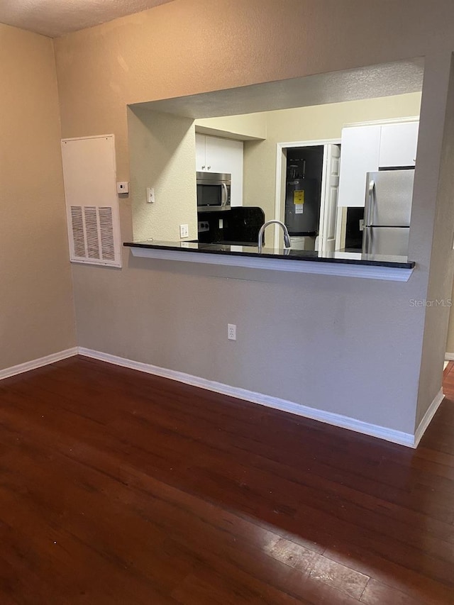 kitchen featuring kitchen peninsula, white cabinets, dark wood-type flooring, and appliances with stainless steel finishes