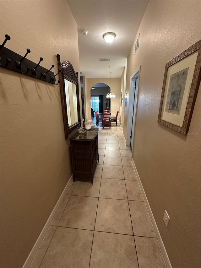 hallway with a textured ceiling and light tile patterned flooring