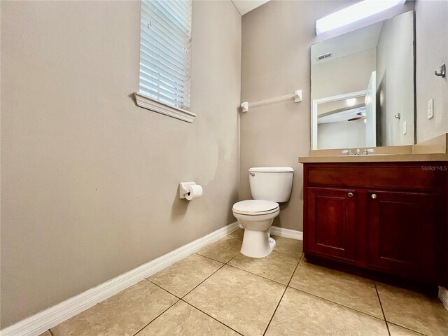 half bath featuring vanity, tile patterned floors, toilet, and baseboards