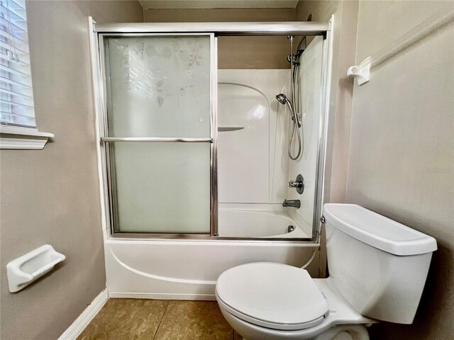 bathroom with tile patterned flooring, toilet, baseboards, and bath / shower combo with glass door