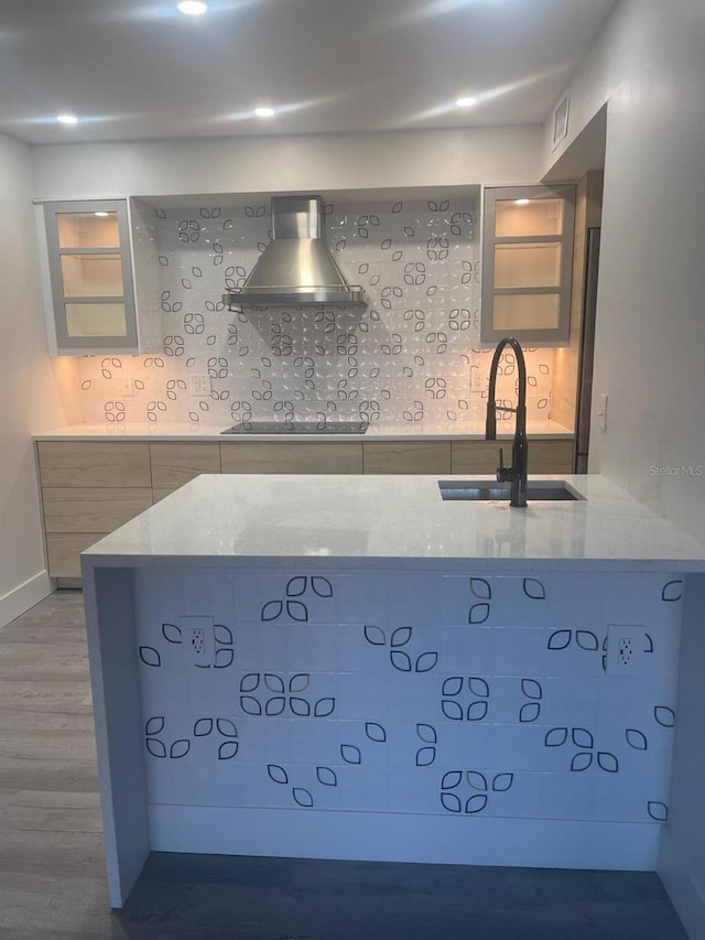 kitchen featuring light stone countertops, sink, wall chimney range hood, wood-type flooring, and decorative backsplash