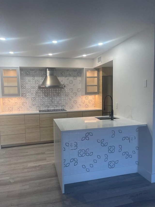 kitchen with kitchen peninsula, backsplash, sink, wall chimney range hood, and hardwood / wood-style flooring