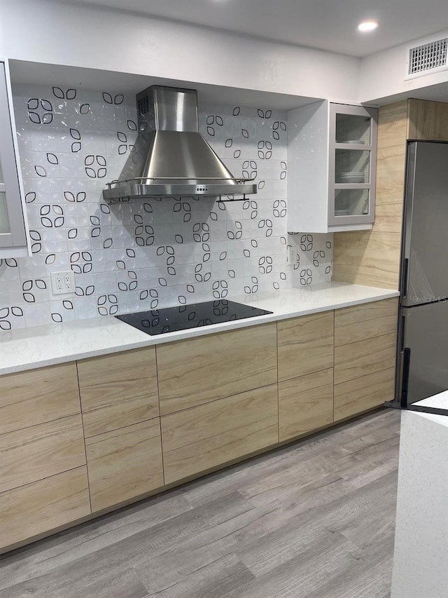 kitchen featuring wall chimney range hood, stainless steel fridge, light hardwood / wood-style floors, decorative backsplash, and black electric stovetop