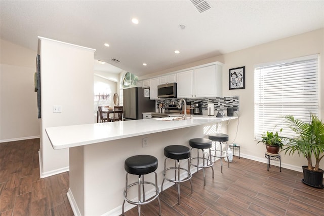 kitchen featuring dark hardwood / wood-style flooring, white cabinetry, a breakfast bar, and stainless steel appliances