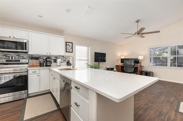 kitchen with dark wood-type flooring, kitchen peninsula, vaulted ceiling, white cabinetry, and stainless steel appliances