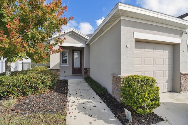 entrance to property featuring a garage, stone siding, fence, and stucco siding