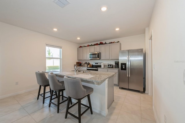 kitchen featuring light stone countertops, appliances with stainless steel finishes, a kitchen island with sink, sink, and a breakfast bar area