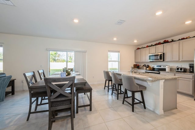 kitchen featuring a center island with sink, plenty of natural light, light stone countertops, and stainless steel appliances