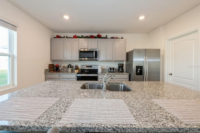 kitchen featuring appliances with stainless steel finishes, light stone counters, sink, a center island with sink, and gray cabinets