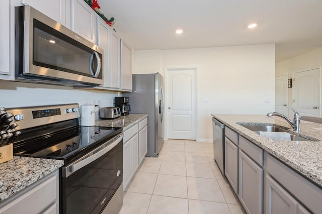 kitchen with gray cabinetry, sink, light tile patterned floors, light stone counters, and stainless steel appliances