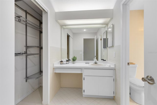 bathroom featuring toilet, vanity, tile patterned floors, and tile walls