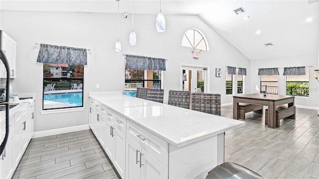 kitchen with kitchen peninsula, light stone counters, pendant lighting, high vaulted ceiling, and white cabinetry